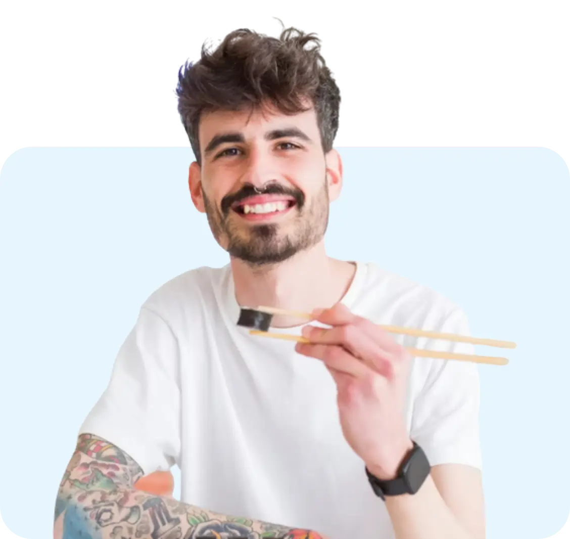 A person with white t-shirt, wearing a watch and holding chopsticks with a piece of sushi, standing against a light blue background.